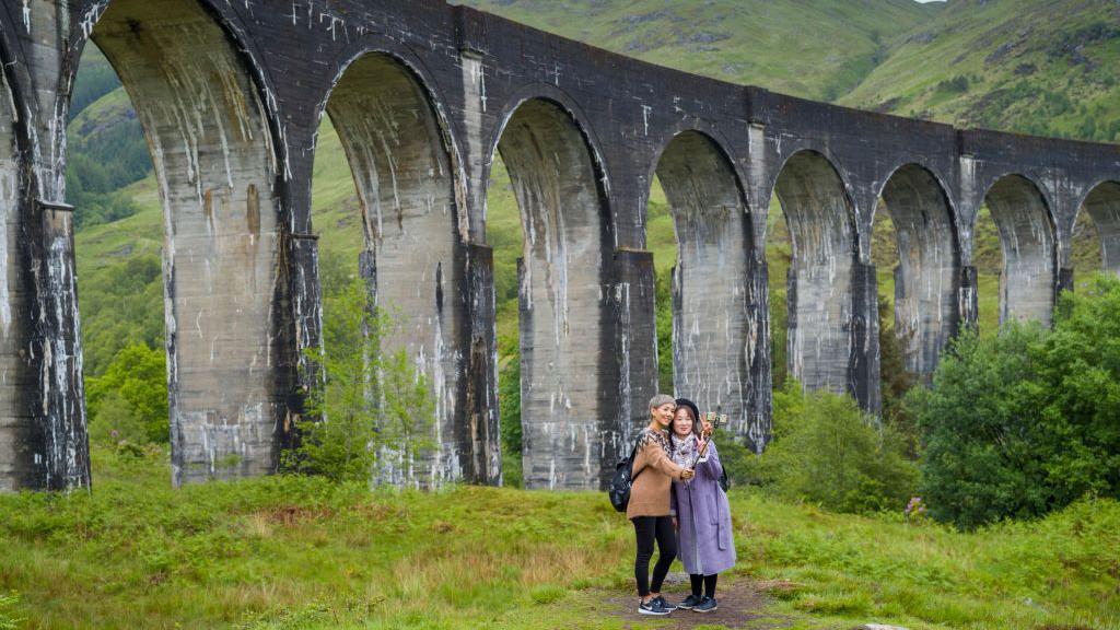 Duas turistas fazendo uma selfie em frente ao Viaduto de Glenfinnan