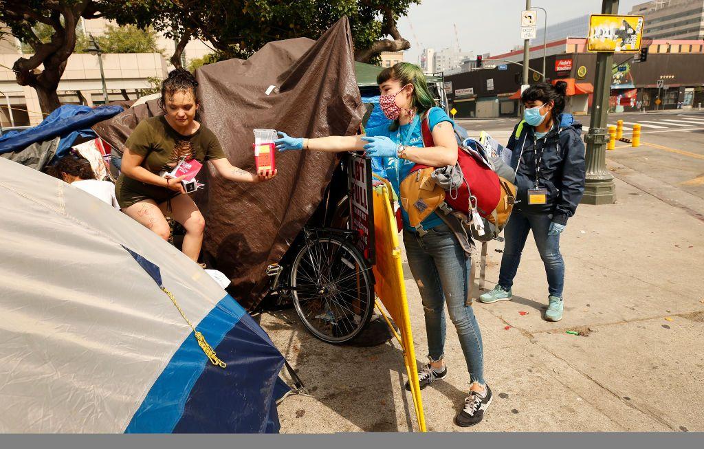 A diretora do programa C3, Ciara DeVozza, à direita, conversa com uma mulher de 20 anos, moradora de rua, em Skid Row, Los Angeles. Enquanto isso, uma equipe de profissionais de saúde realiza testes de COVID-19 em desabrigados na região