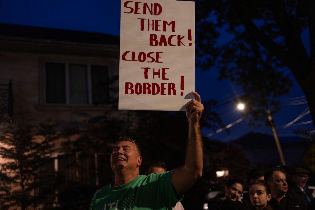 Residentes locais e ativistas anti-imigrantes reúnem-se para o oitavo protesto contra o uso da escola fechada St. John Villa Academy em Staten Island, Nova Iorque, como abrigo para migrantes. Um homem de camiseta verde segura uma placa com a frase: 