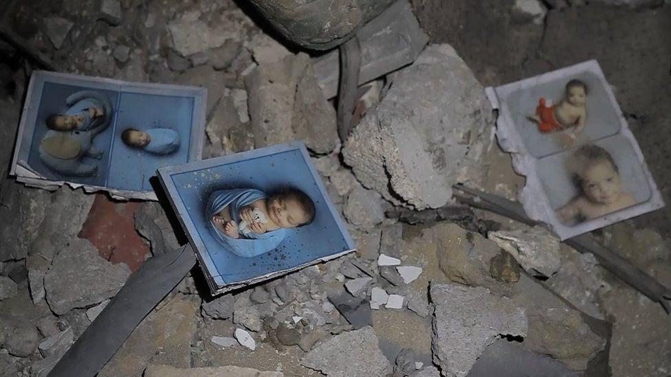 Wide shot of five photos of a baby, strewn over the rubble in Gaza City's St Porphyrius Church