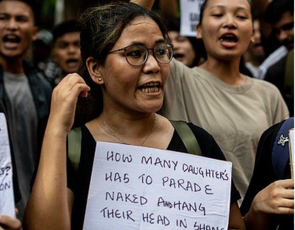 Una mujer con una pancarta que dice: Cuántas de nuestras hijas tienen que ser exhibidas desnudas