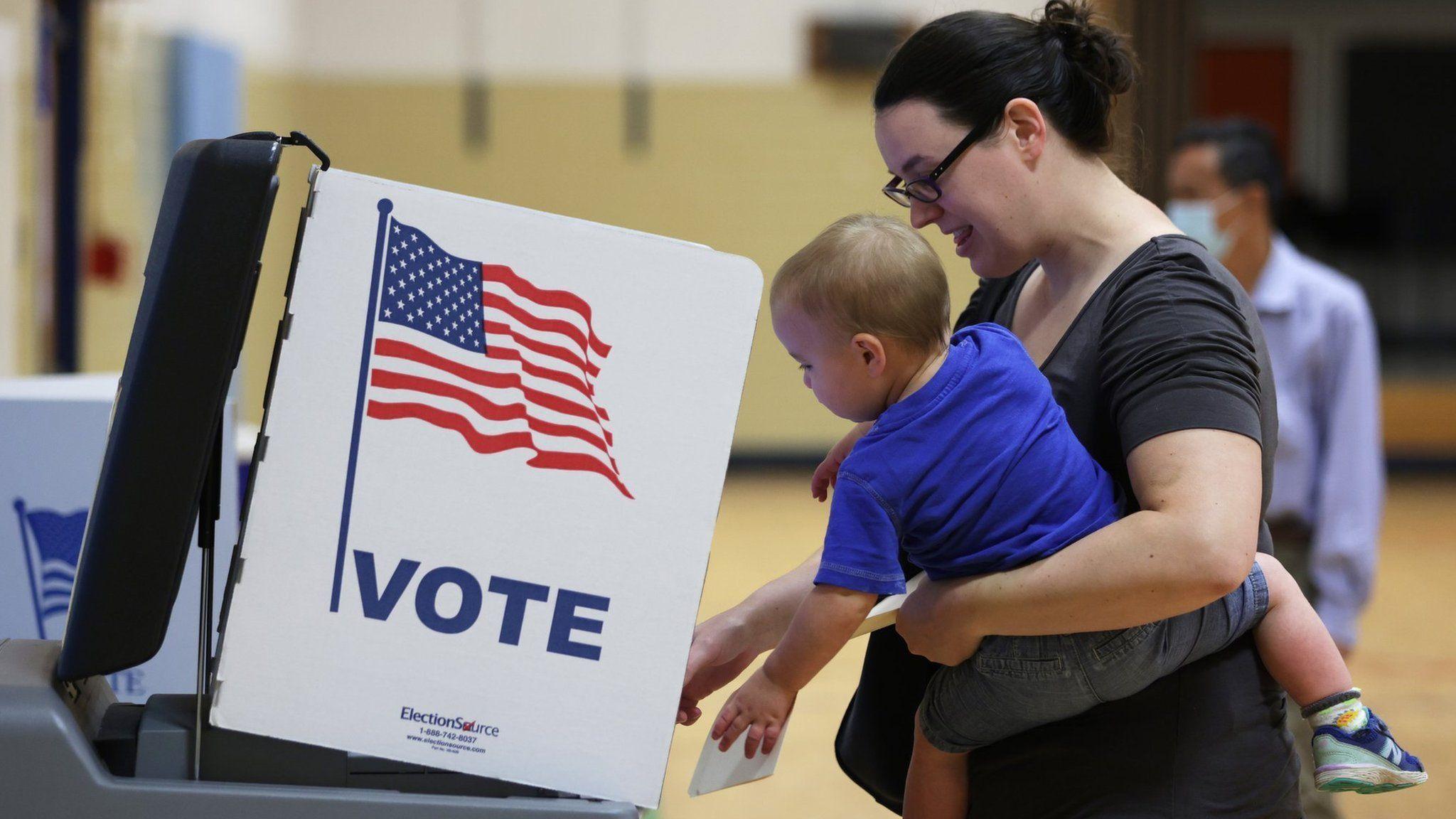 Uma mulher vota nas primárias dos Estados Unidos na Virgínia, com uma criança no colo