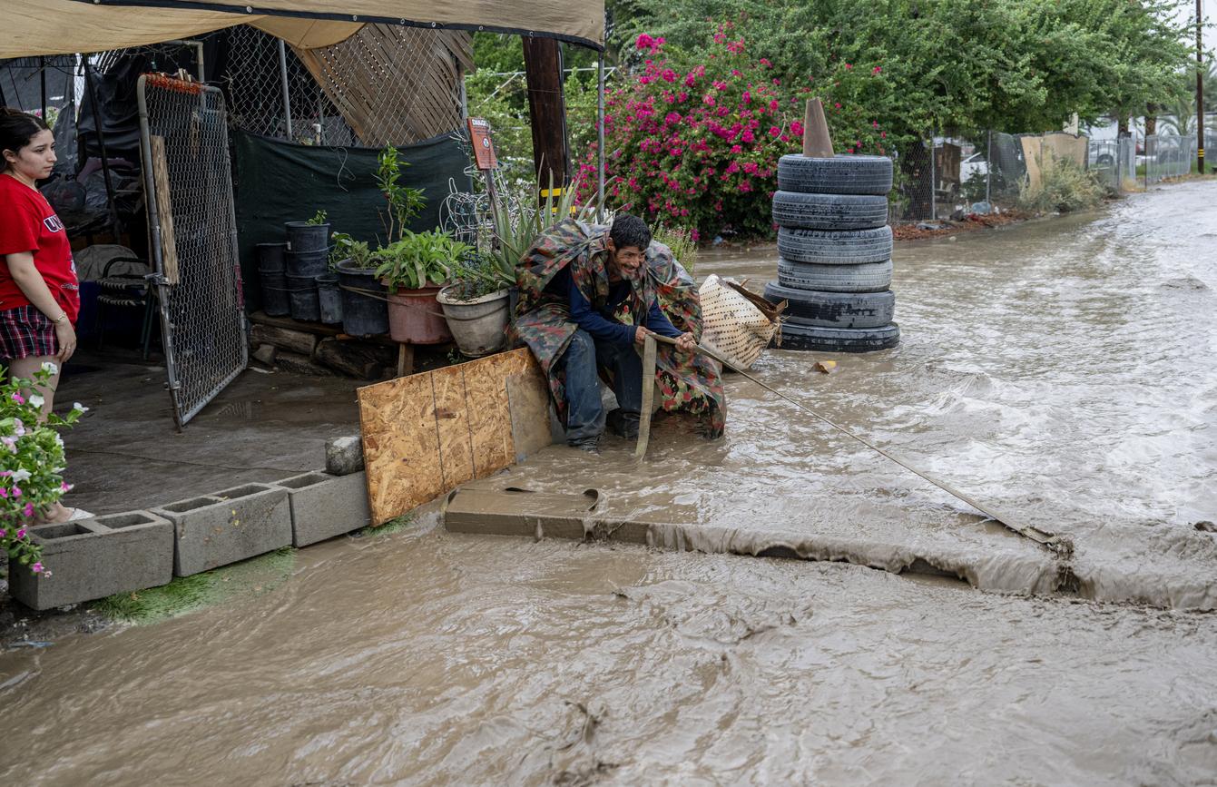 Sergio López arrastra una gran tabla de madera al frente de la casa rodante de su amigo para ayudar a desviar el agua de la inundación que corre durante la tormenta tropical Hilary en Thermal, California.