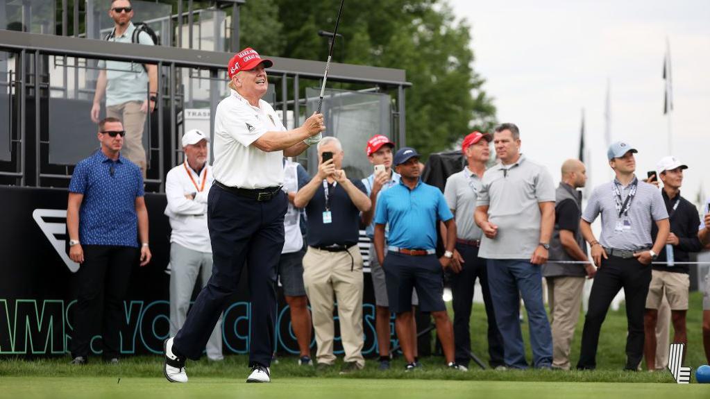 Donald Trump jugando al golf delante de otros jugadores y miembros del Servicio Secreto.