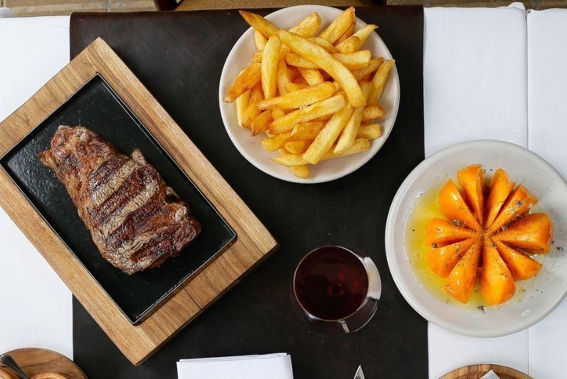 Carne, batatas fritas e prato com algo laranha vistos de cima