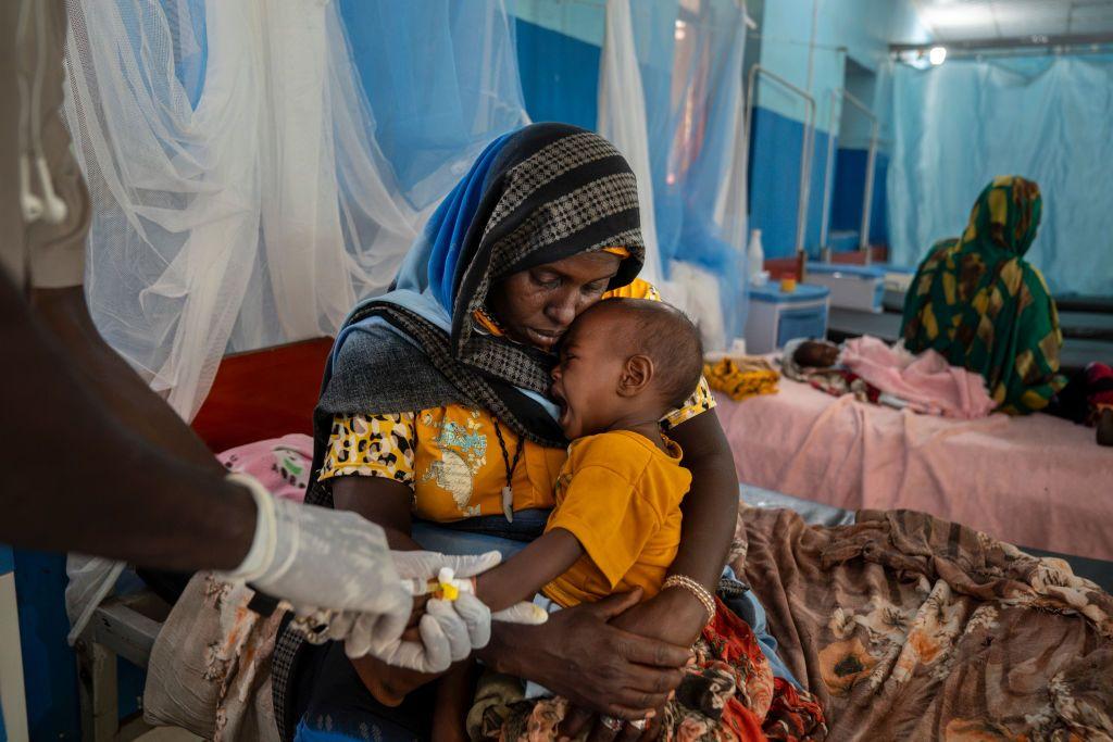 أم تحمل طفلها الذي يعاني من سوء التغذية، بعد تلقيه العلاج في مستشفى بولاية غرب دارفور