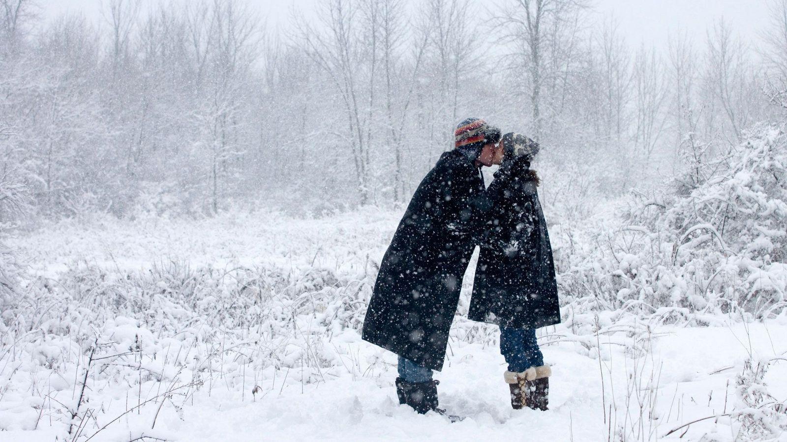 Dos personas se besan en un bosque mientras cae la nieve