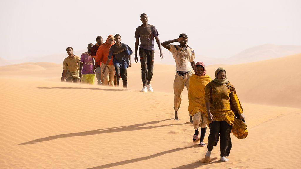 Pessoas caminham em fila no deserto em cena do filme Eu, Capitão