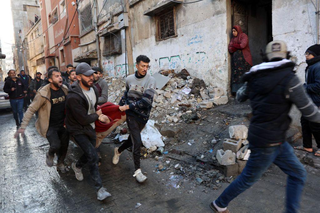 فلسطينيون يحملون جثة ضحية من بين أنقاض مبنى دمر في غارات جوية إسرائيلية في مدينة غزة في 13 يناير/كانون الثاني 2025. الصورة التقطت نهاراً.