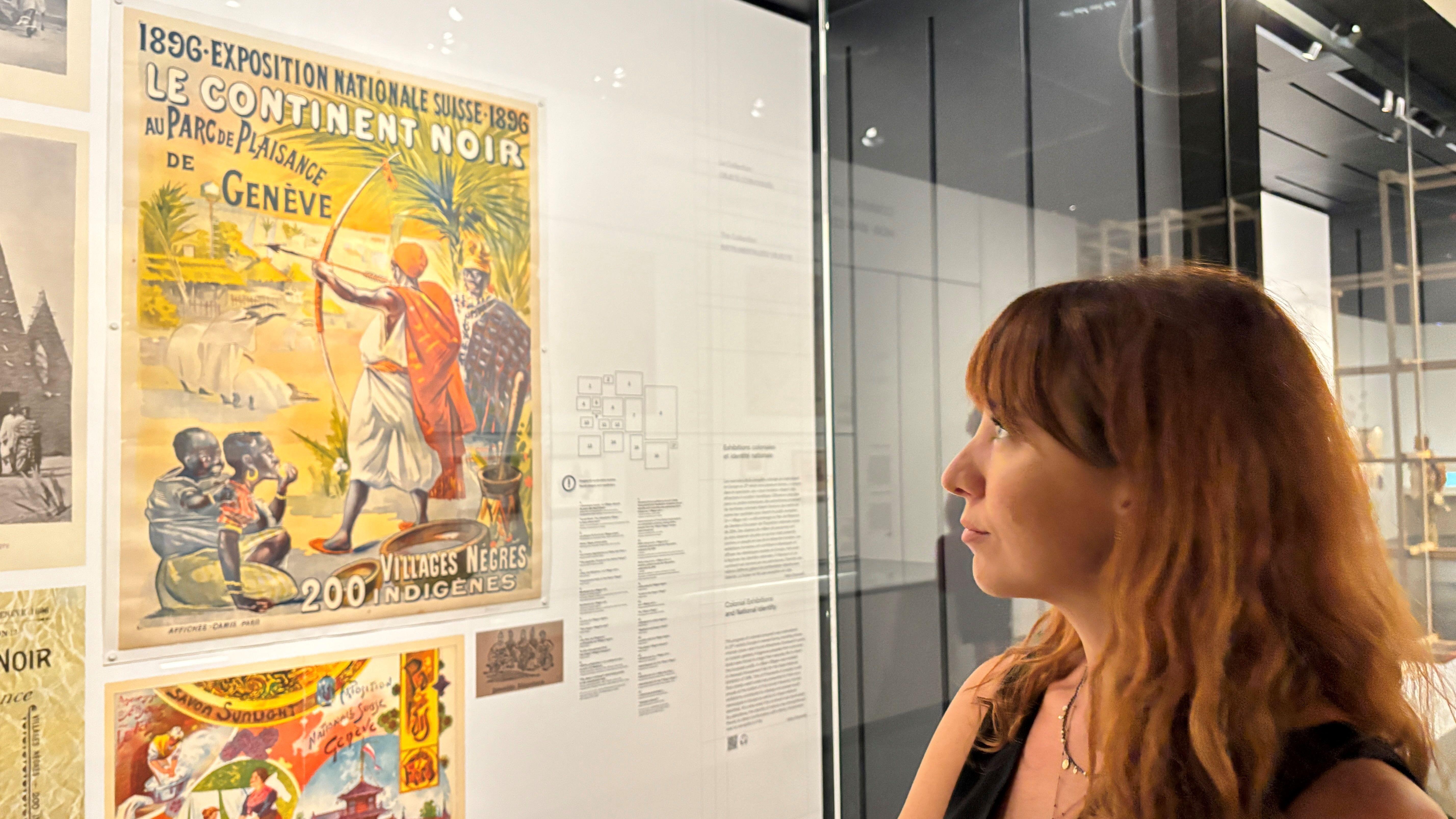 Letizia Pinoja observando um pôster vintage na exposição que analisa o passado colonial da Suíça.