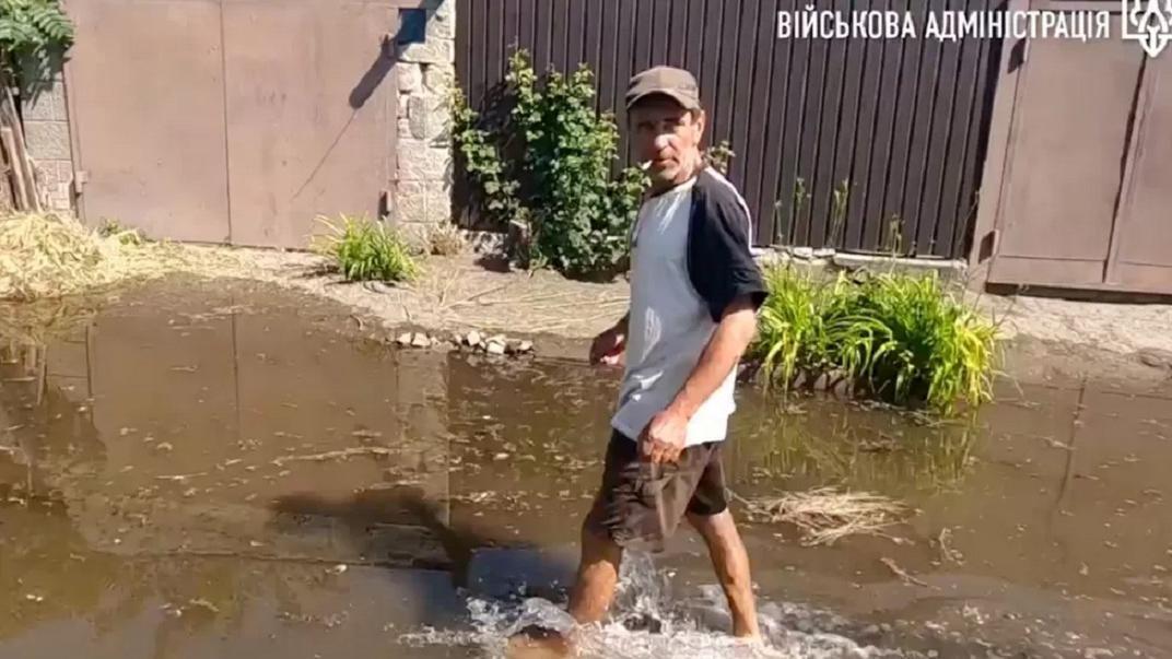 Seorang pria menerabas banjir di Kherson - sebuah kota yang terletak di tepi barat Dnipro.