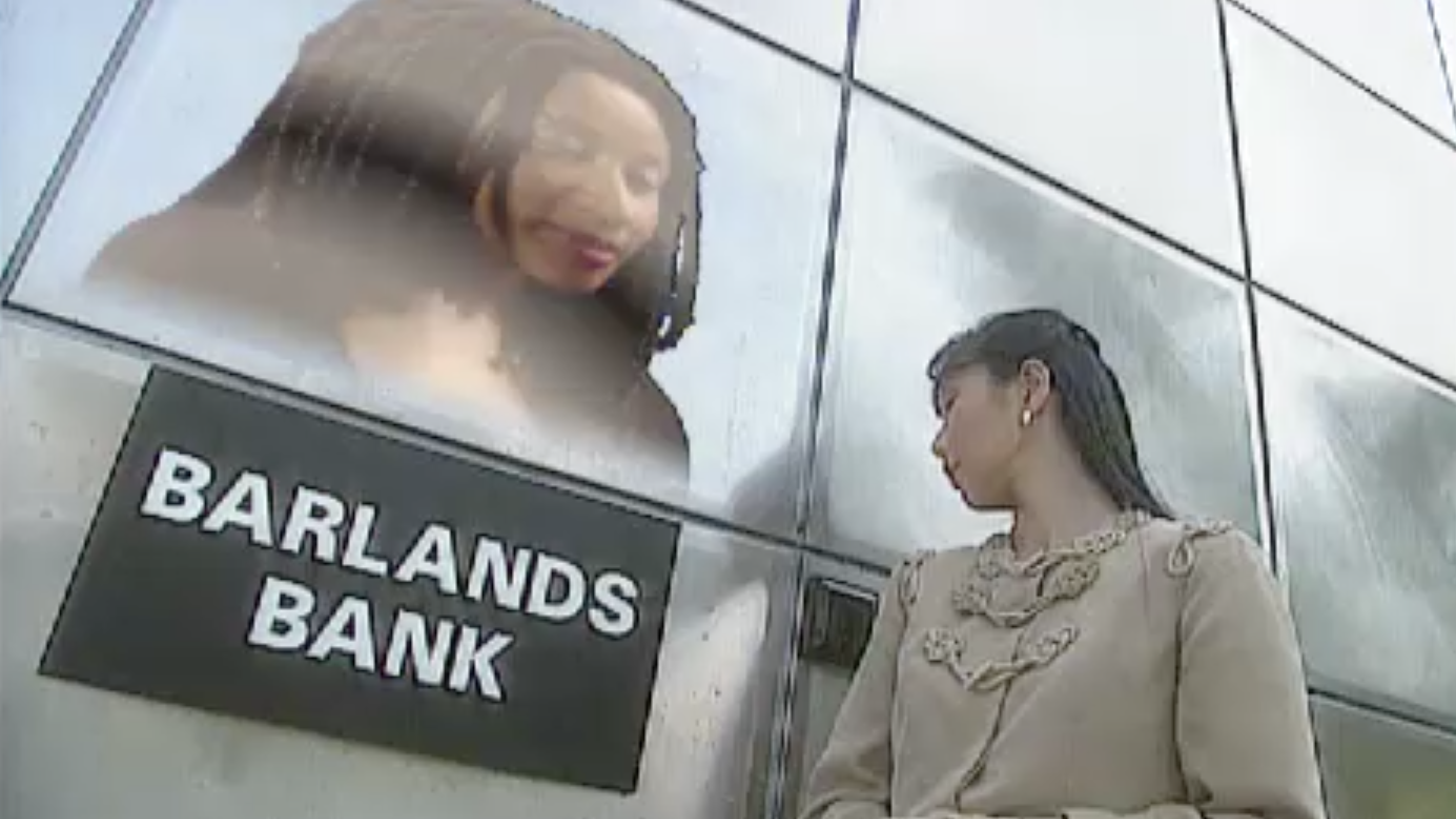 Uma mulher em um banco do futuro, falando com um holograma com a placa Barlands Bank.