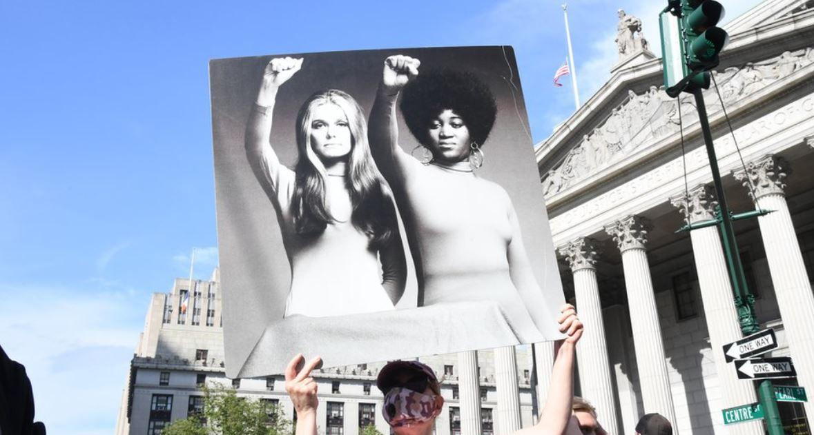 Una persona alza la imagen de Gloria Steinem y Angela Davis  con los puños en alto