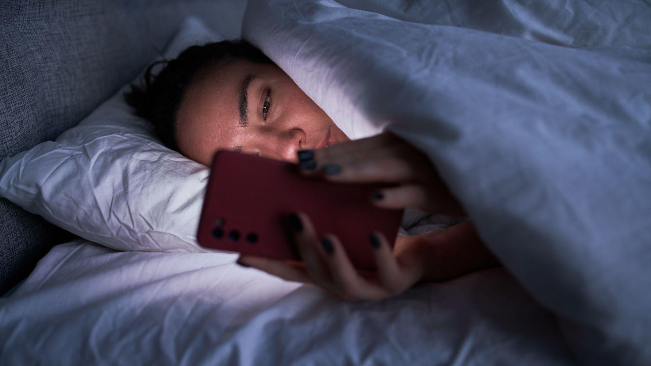 Una mujer viendo su celular en la cama
