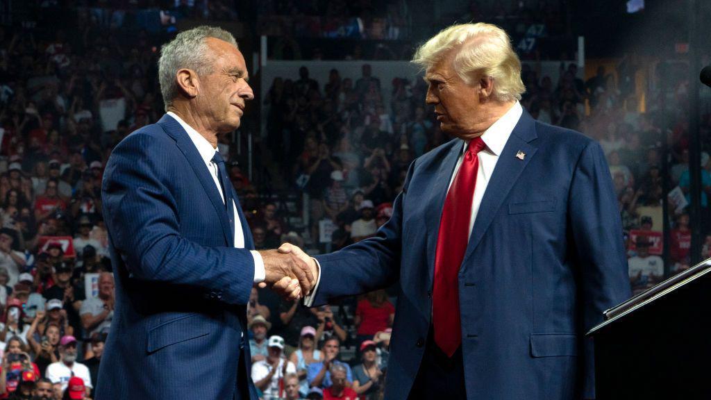 Robert Kennedy Jr. e Donald Trump apertam as mãos.