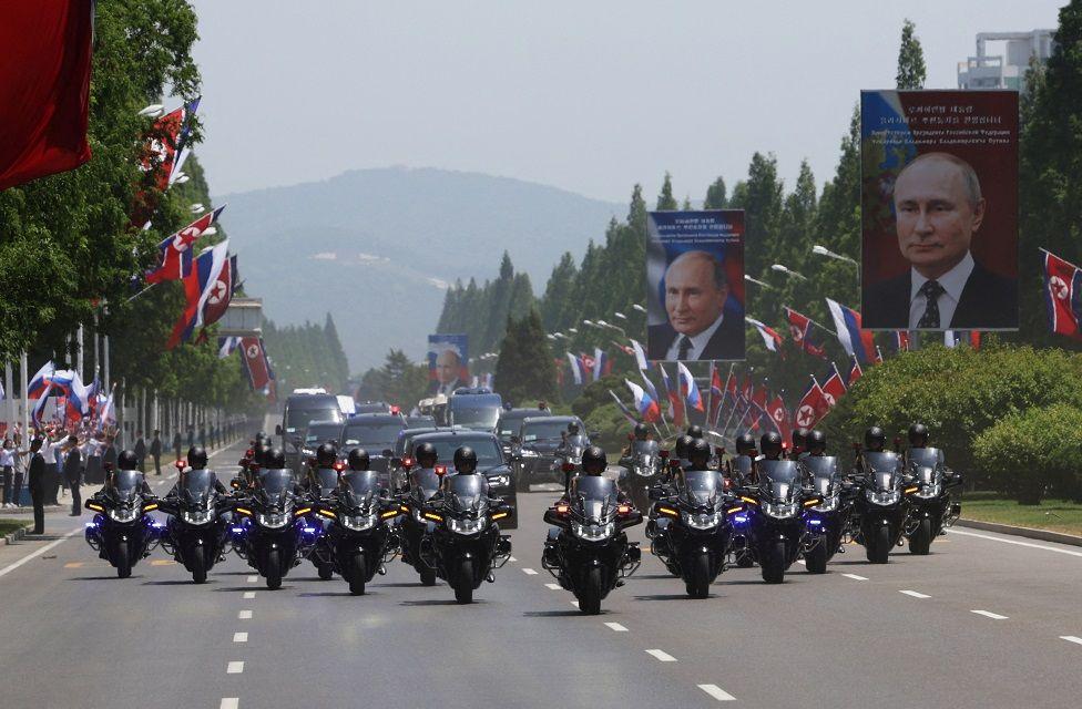 Un contigente de motorisados en una gran avenida. A los lados se ven banderas de Rusia y Corea del Norte y fotos gigantes del presidente ruso, Vladimir Putin