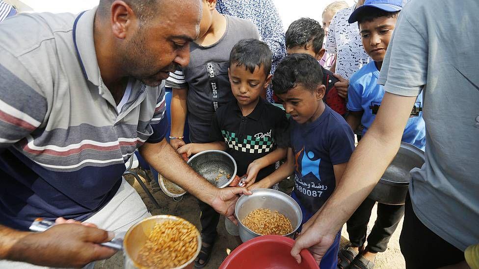 Niños y adultos esperando por un plato de comida en un centro de UNRWA