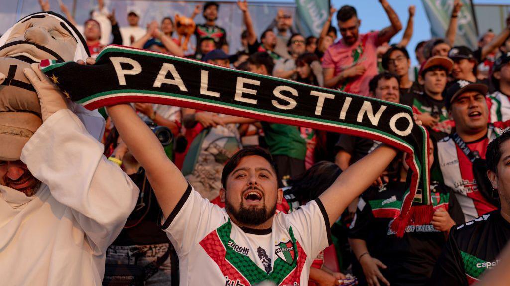 Homem em torcida ergue faixa onde se lê: 'Palestino'