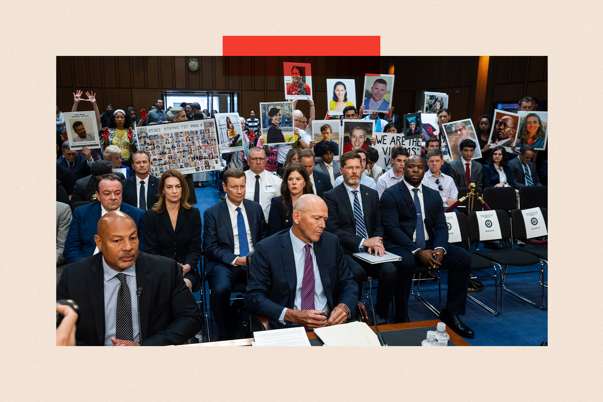 People with placards sit behind then-Boeing CEO, David Calhoun