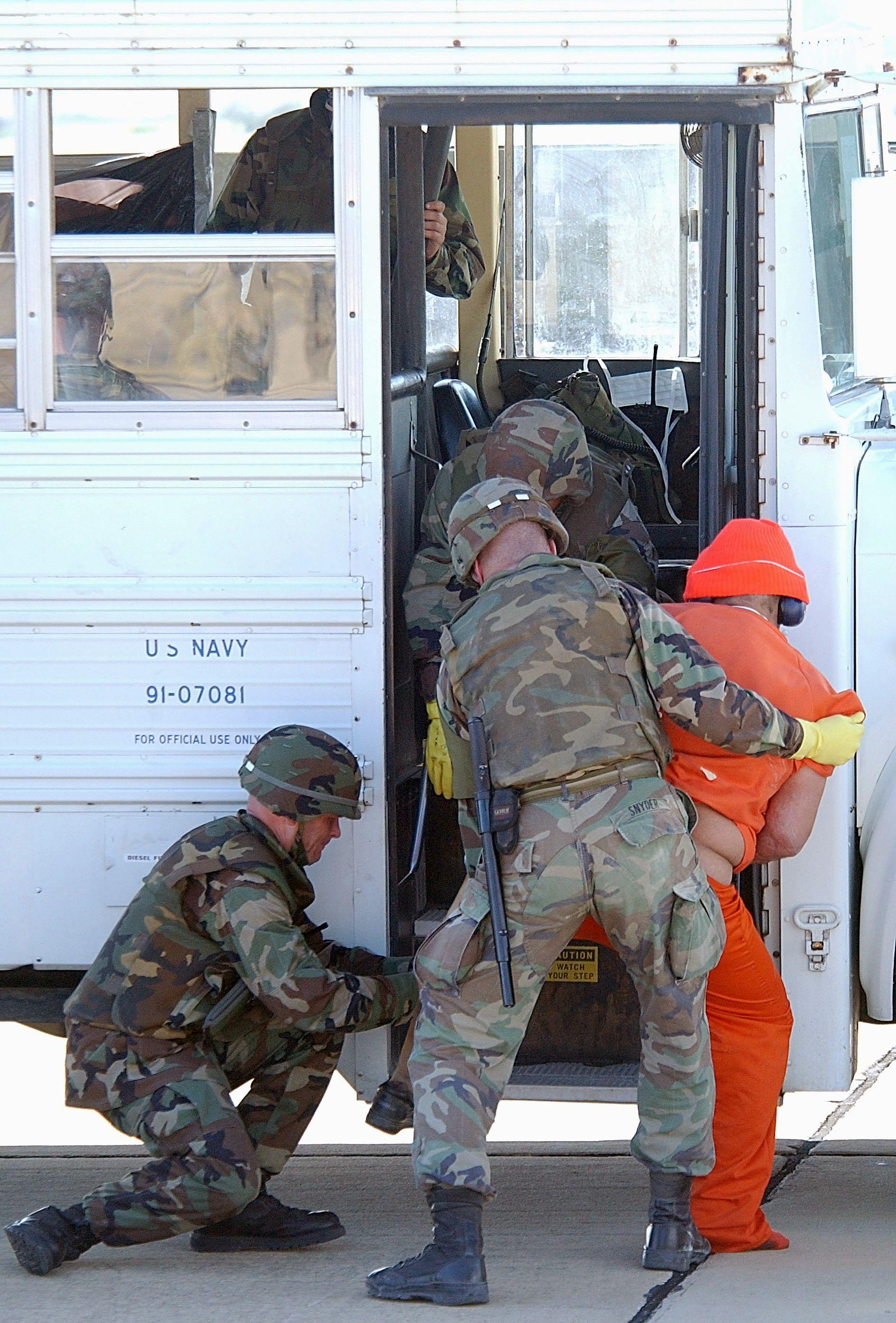 Soldados ayudan a un detenido a subir a un autobús.