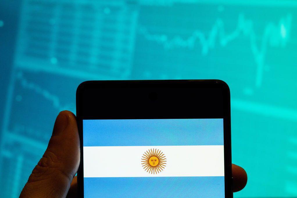 Un celular con una imagen de la bandera argentina frente a un gráfico de la bolsa.