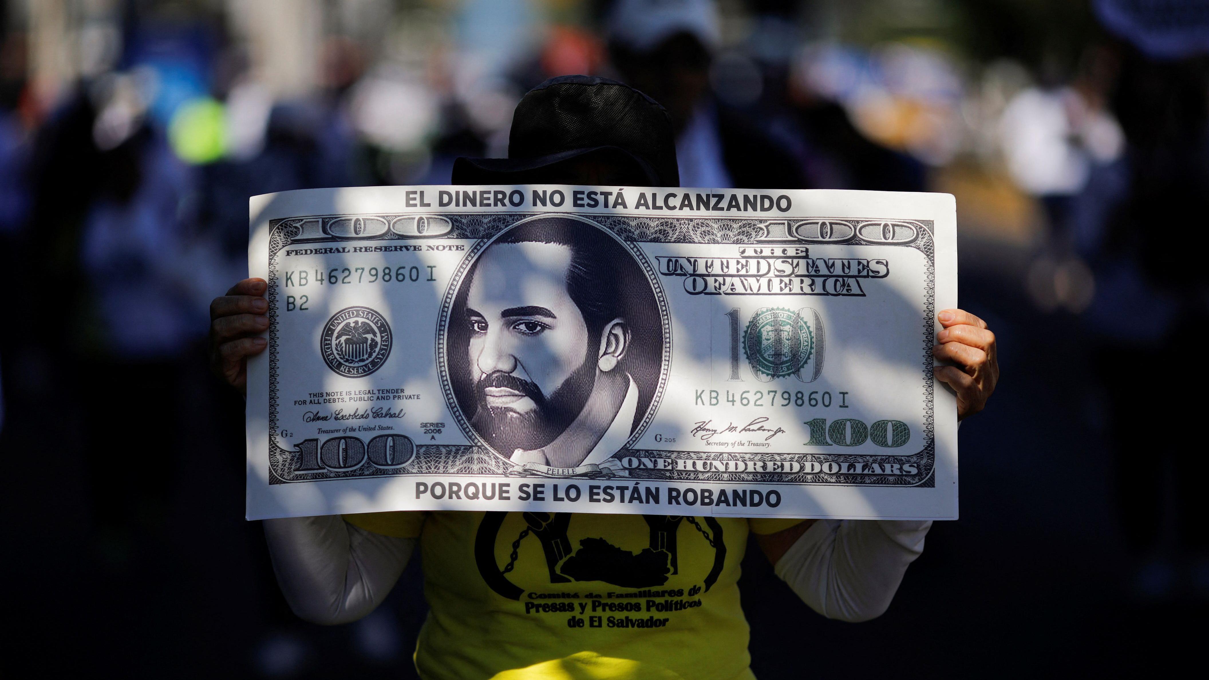 Una manifestante sostiene un cartel que representa un billete de 100 dólares con el rostro del presidente Nayib Bukele impreso y el mensaje "El dinero no está alcanzando porque se lo están robando"  durante una protesta en San Salvador, El Salvador, el 23 de noviembre de 2024. REUTERS/José Cabezas
