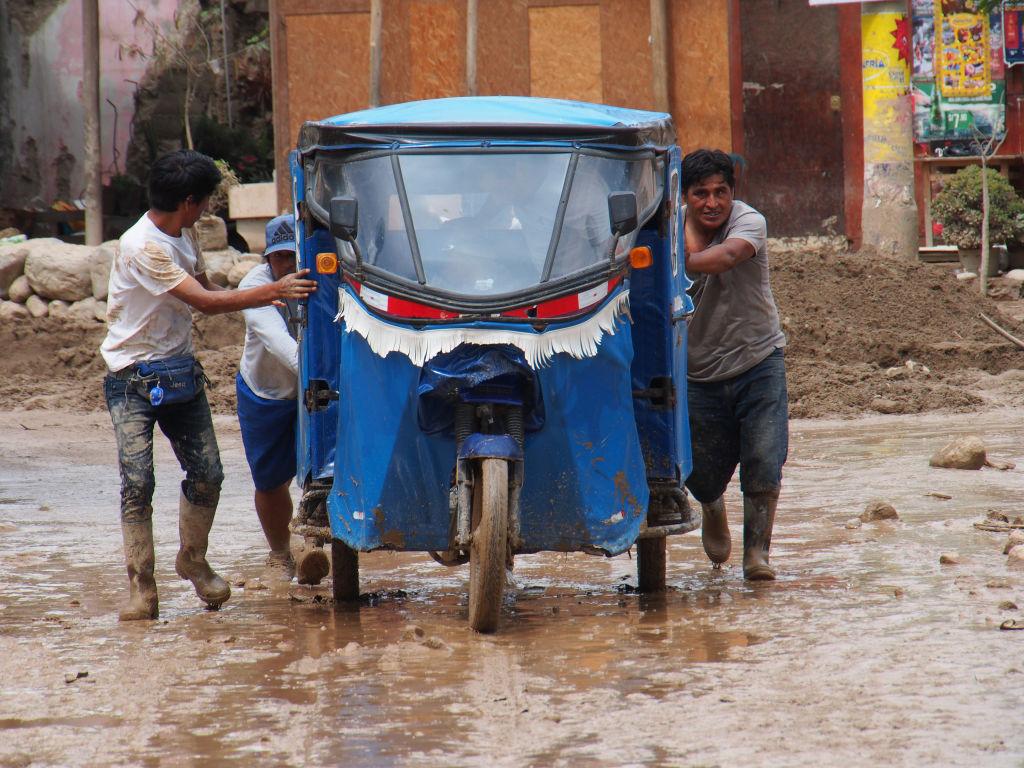 Tres hombres empujan un mototaxi en Lima.
