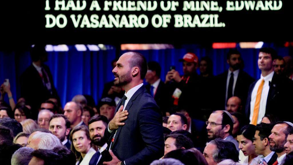 Eduardo Bolsonaro em p&eacute; enquanto o presidente dos EUA, Donald Trump fala durante a Confer&ecirc;ncia de A&ccedil;&atilde;o Pol&iacute;tica Conservadora