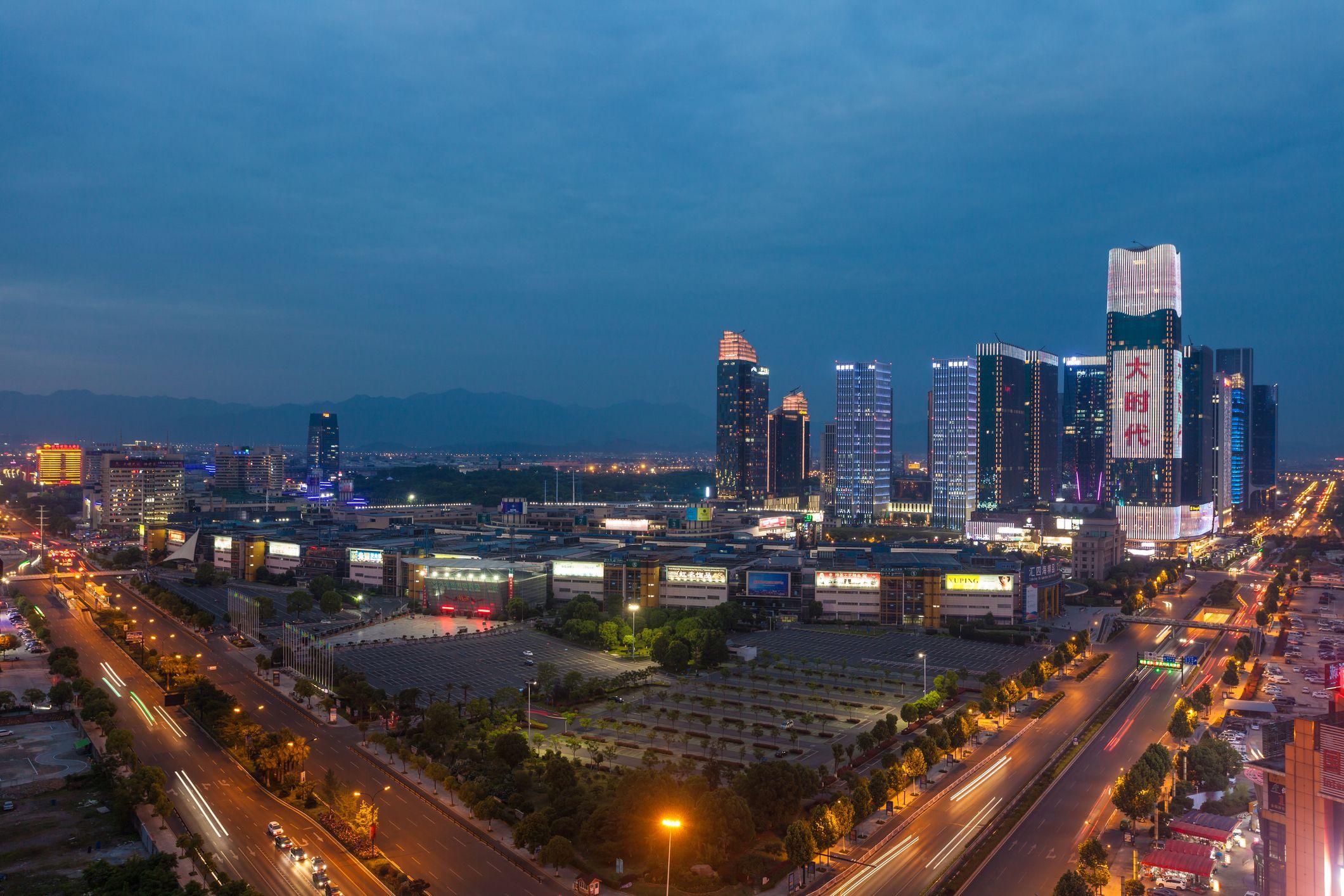 Foto panorâmica de cidade Yiwu à noite, de onde se pode ver prédios iluminados e avenidas