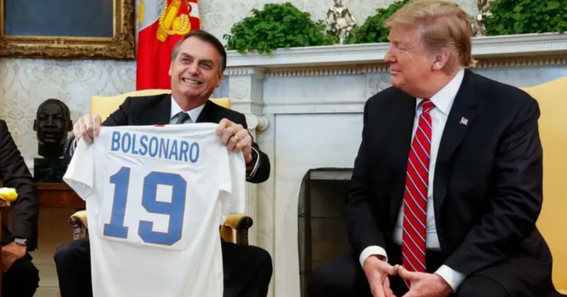 Bolsonaro segura uma camisa de futebol com seu nome enquanto Donald Trump observa