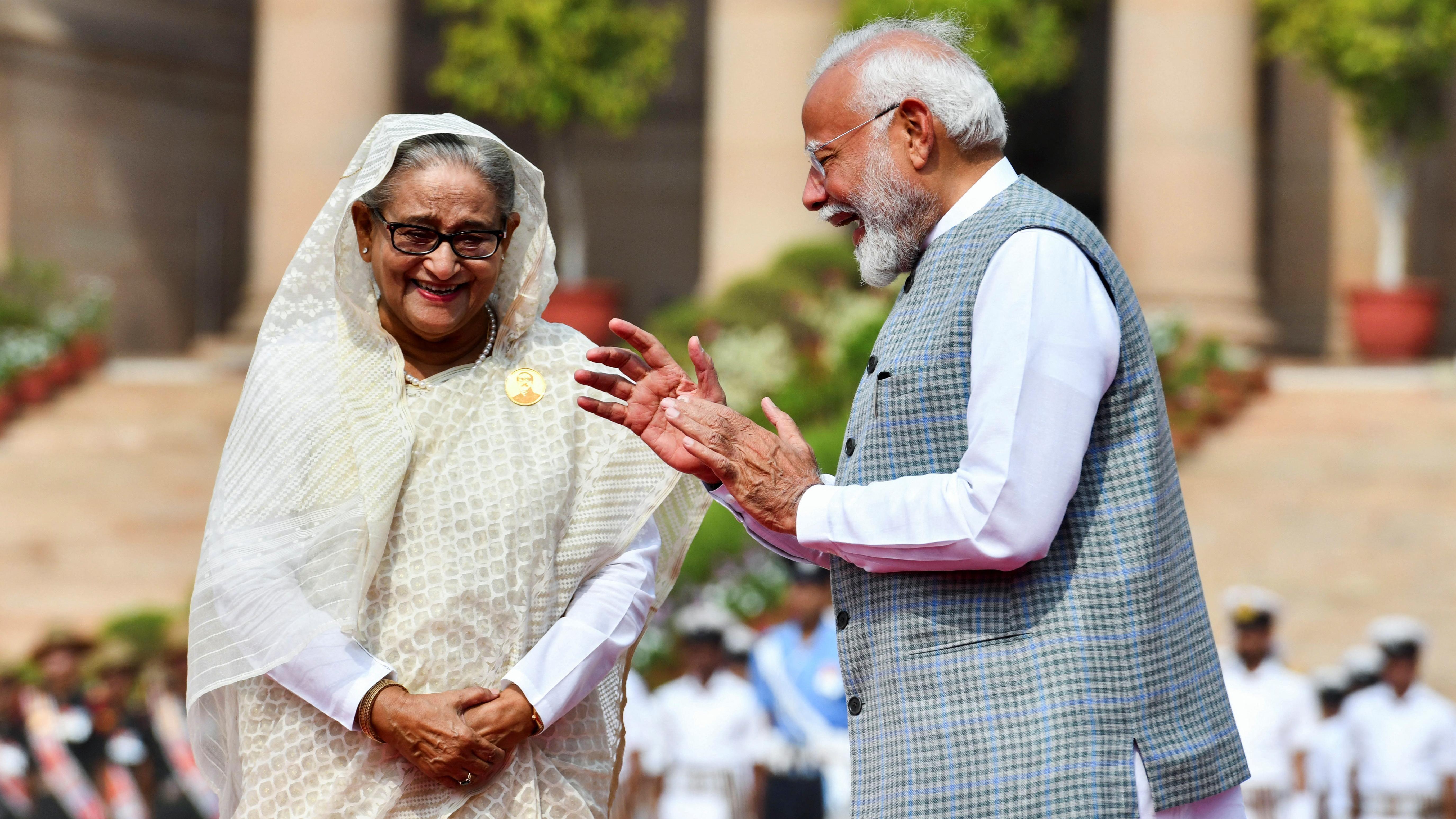 Sheikh Hasina, primeira-ministra de Bangladesh, sorri em um sári branco e creme enquanto fala com seu homólogo indiano, Narendra Modi, que também está rindo em um colete xadrez nehru