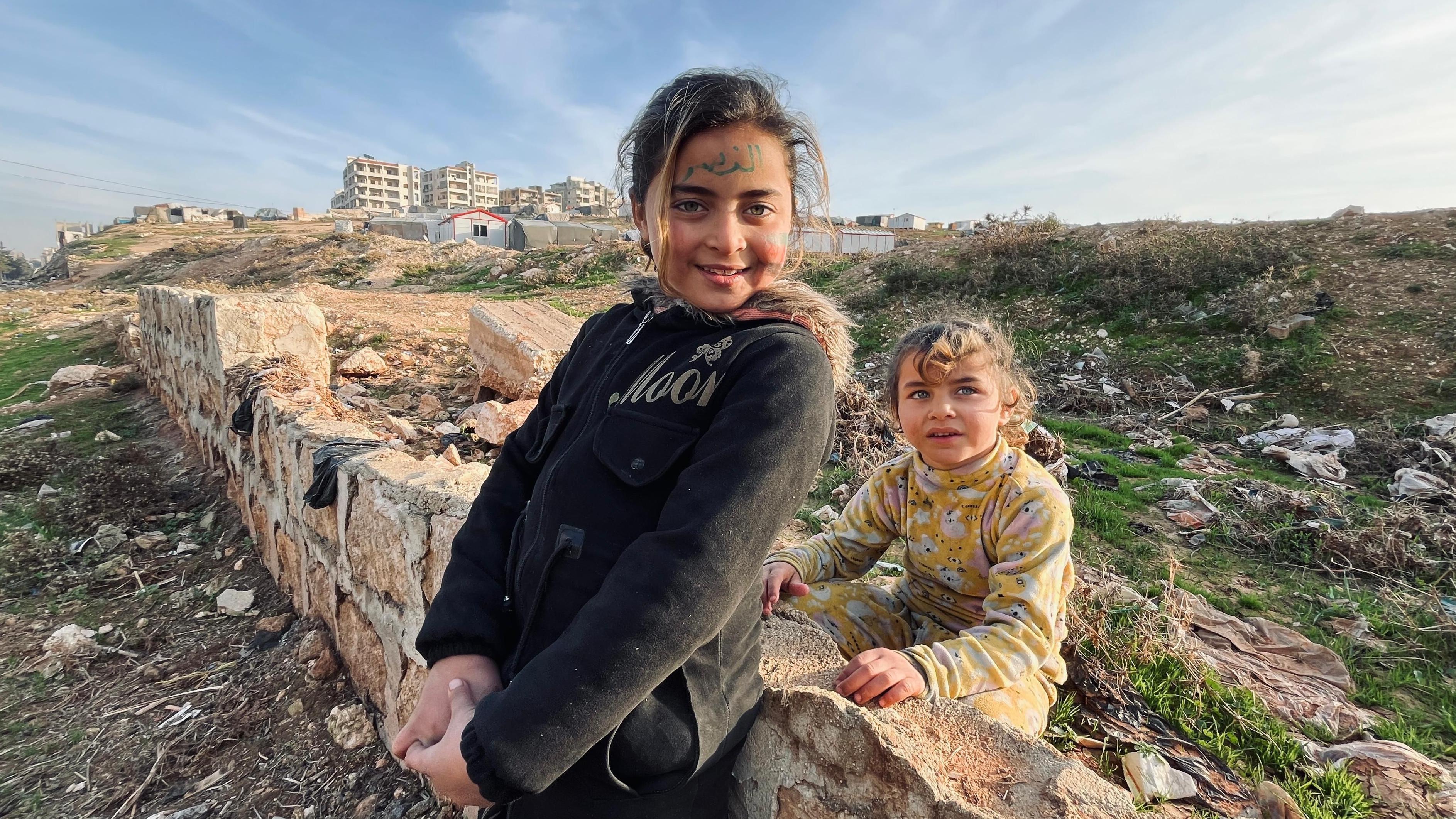 Duas meninas encostadas em um muro destruído em Idlib