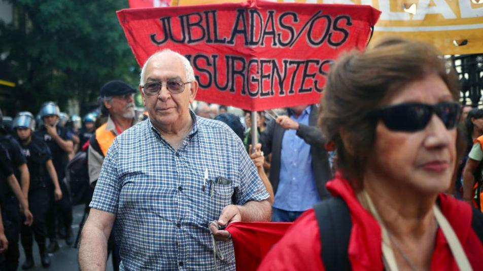 Un hombre y una mujer participan de una "marcha de los jubilados" con un cartel que dice "Jubilados insurgentes"