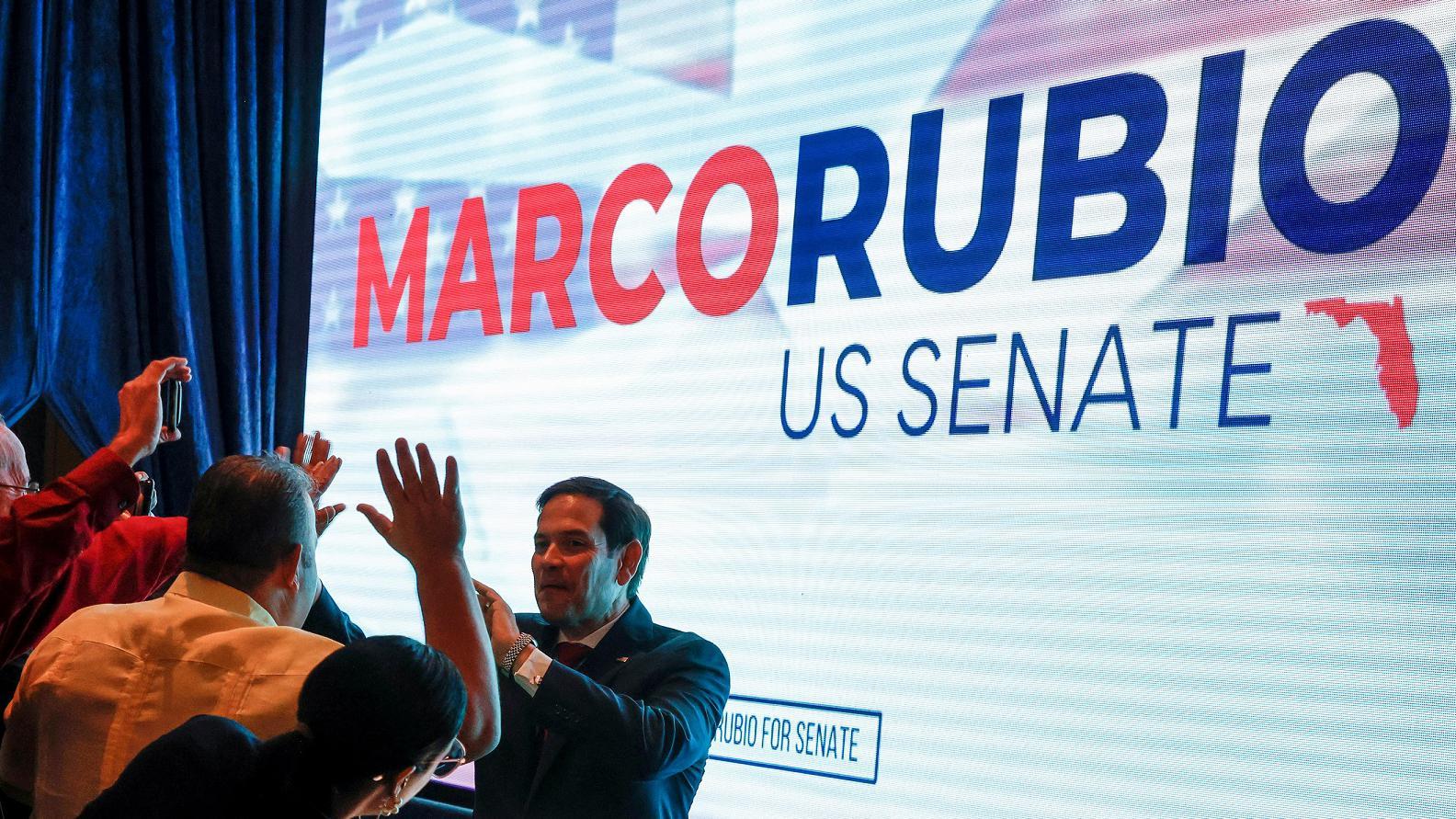 Marco Rubio em frente a telão com seu nome, cumprimentando apoiadores