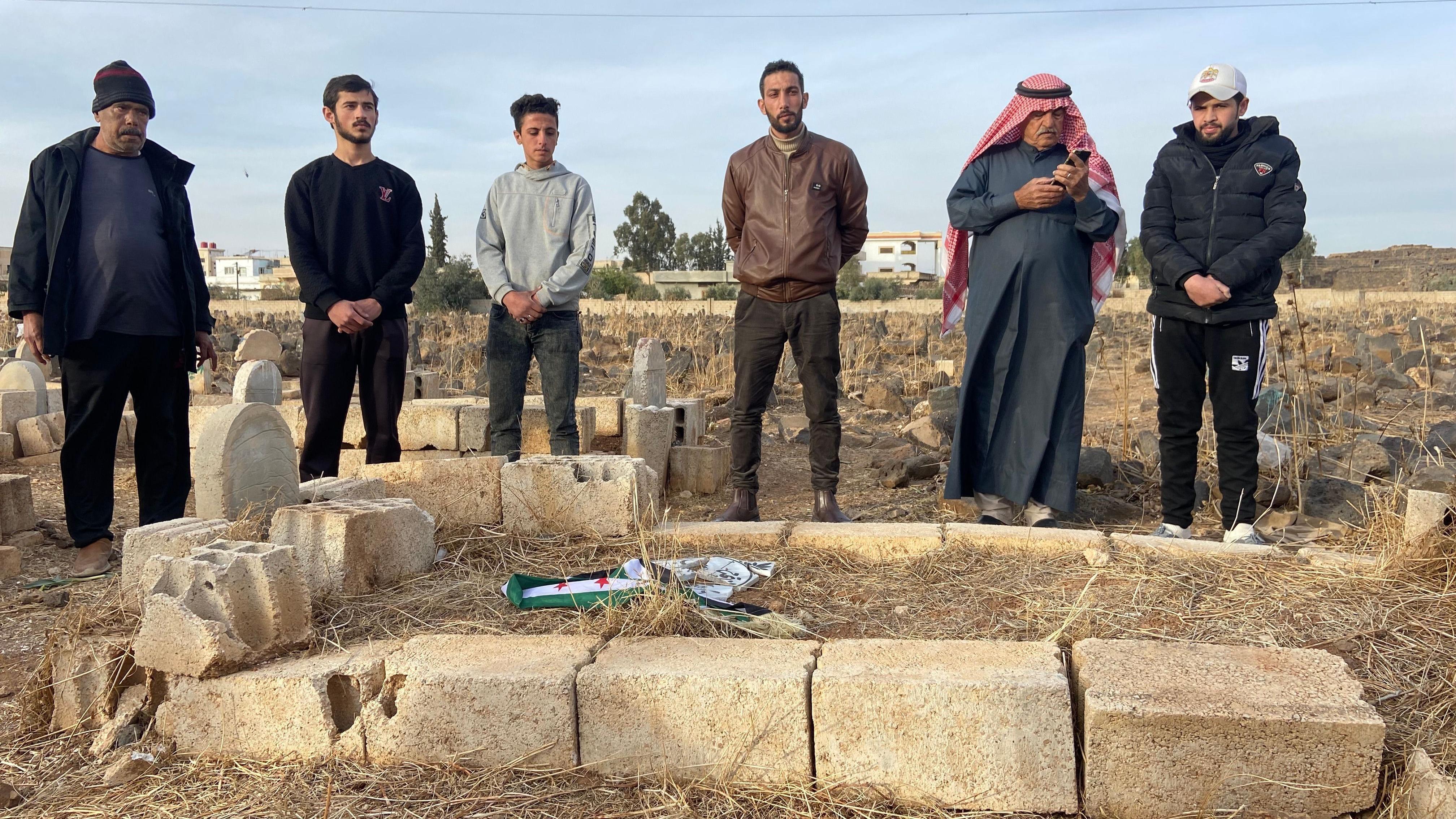 Hamza'nın mezar taşına Suriye muhalefeti bayrağı sarılırken, sessizce izleyen komşuları. e.
