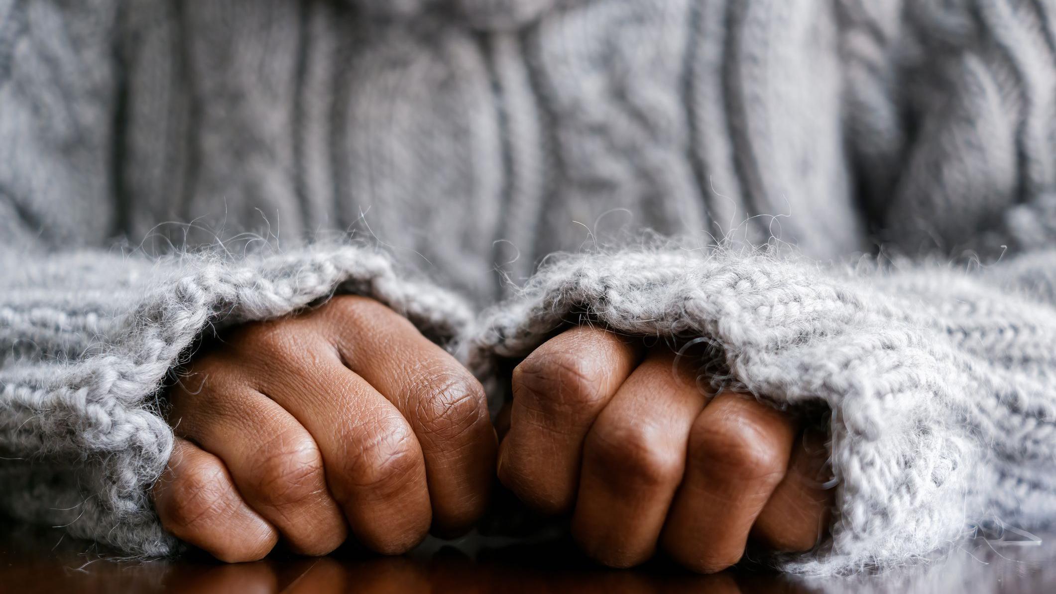 Foto de banco de imagem mostra as mãos de mulher fechadas em cima de uma mesa de madeira