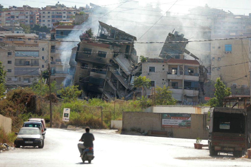 Un hombre en moto circula cerca de un edificio bombardeado por Israel.