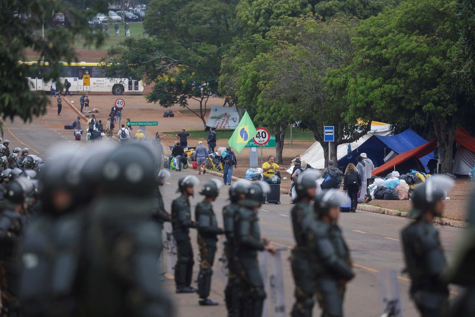 Dezenas de policiais observam manifestantes em verde e amarelo desmantelando acampamento