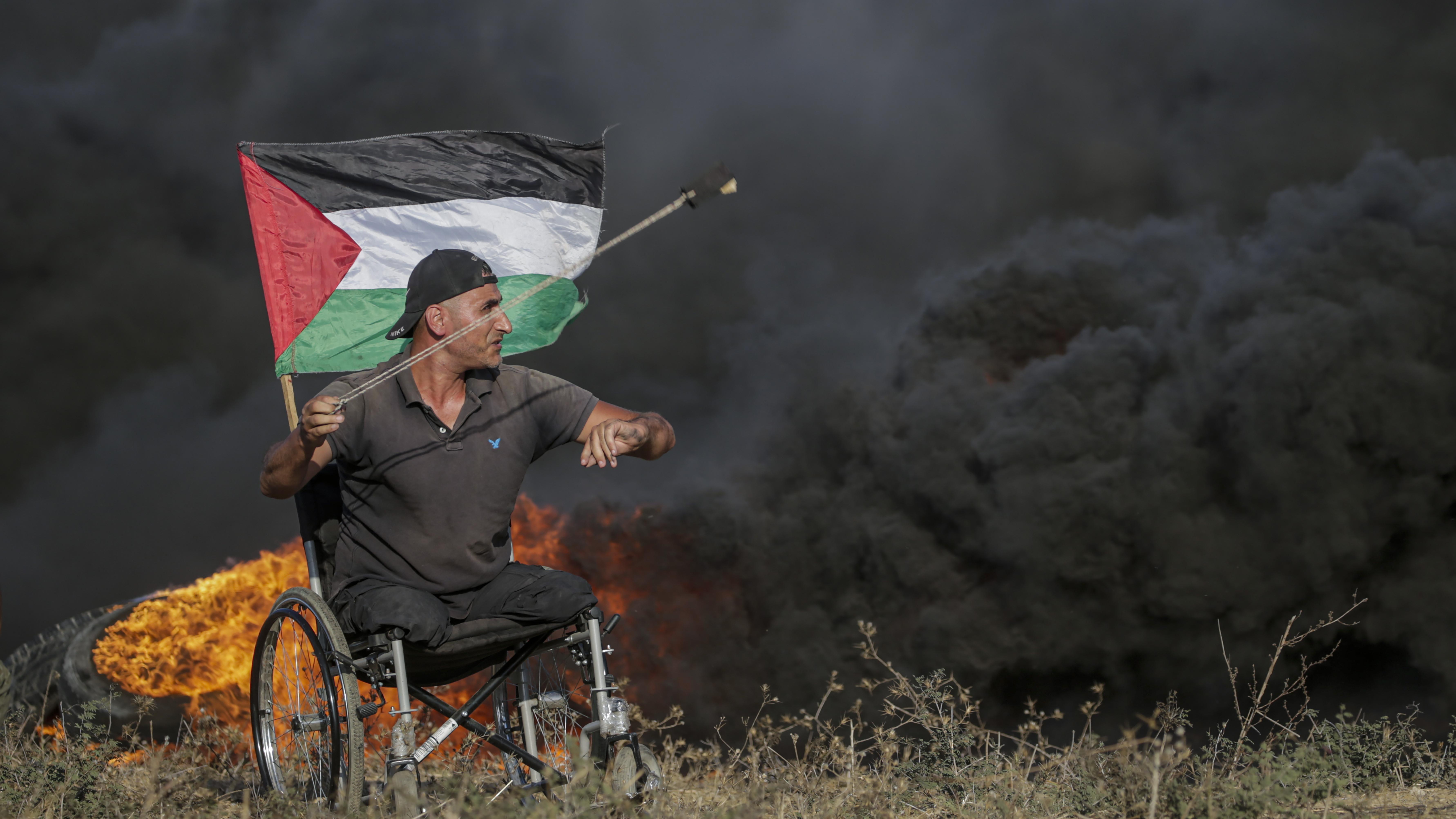 متظاهر فلسطيني مبتور الأطراف على كرسي متحرك يلقي الحجارة على القوات الإسرائيلية خلال اشتباكات على الحدود الشرقية لقطاع غزة.