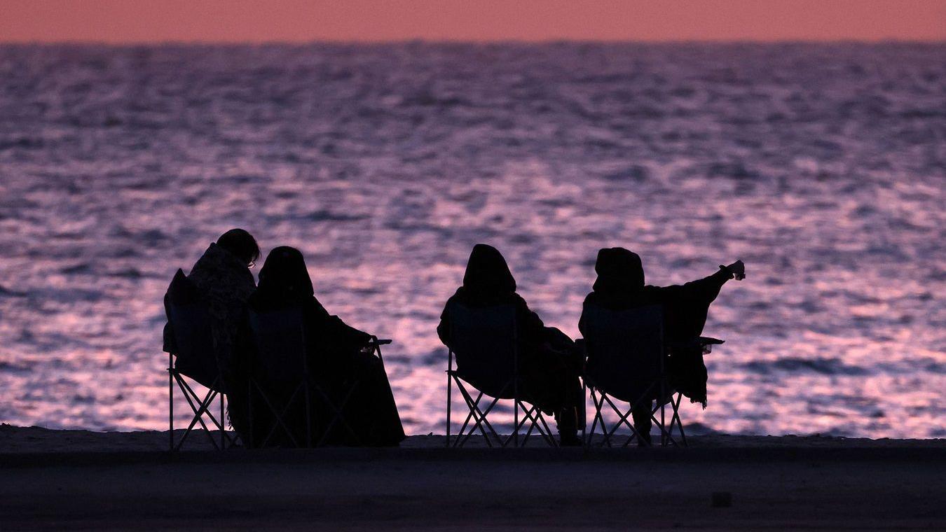 نساء يجلسن على الشاطئ عند شروق الشمس في مدينة الكويت في 15 أبريل 2023
