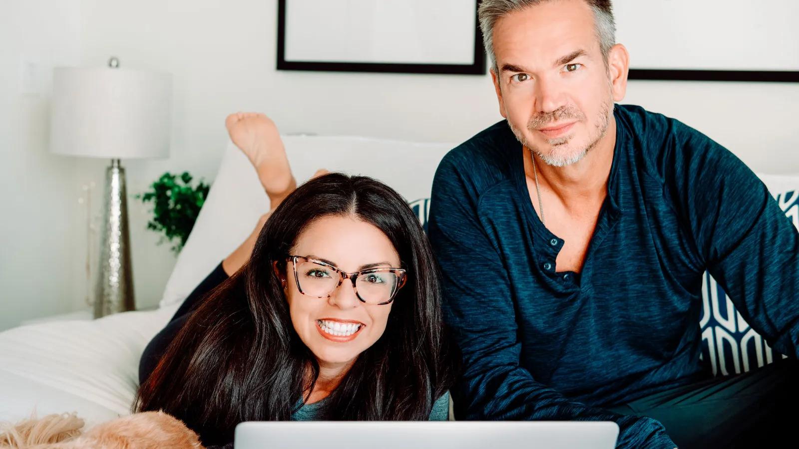 Casal em cima da cama olhando laptop