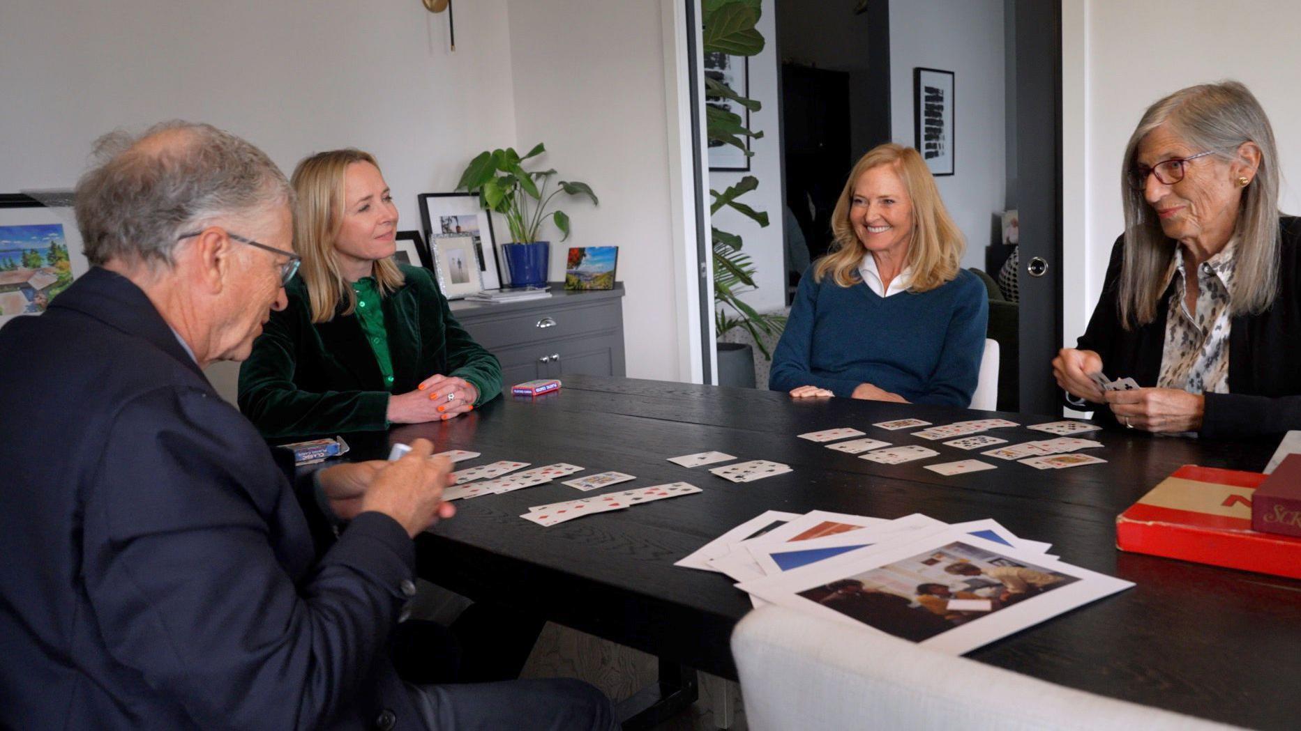 (De izquierda a derecha) Perfil lateral de Bill Gates sosteniendo cartas, Katie Razzall sonriendo, con las hermanas de Bill, Libby y Kristi, que está jugando a las cartas. 