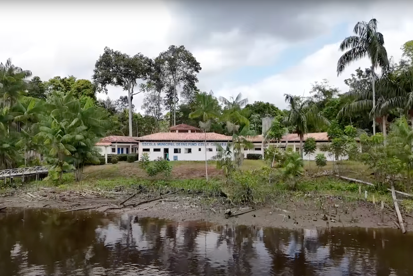 Edifício escolar na beira do rio, com floresta ao fundo