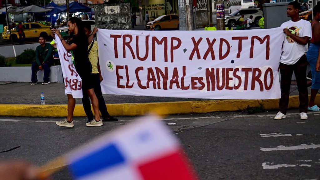 Dos hombres sostienen una pancarta que dice "Trump el canal es nuestro"