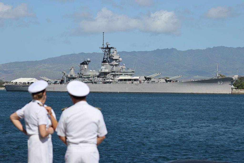 Tres marineros conversan con un buque de guerra de Estados Unidos de fondo en Hawái. 