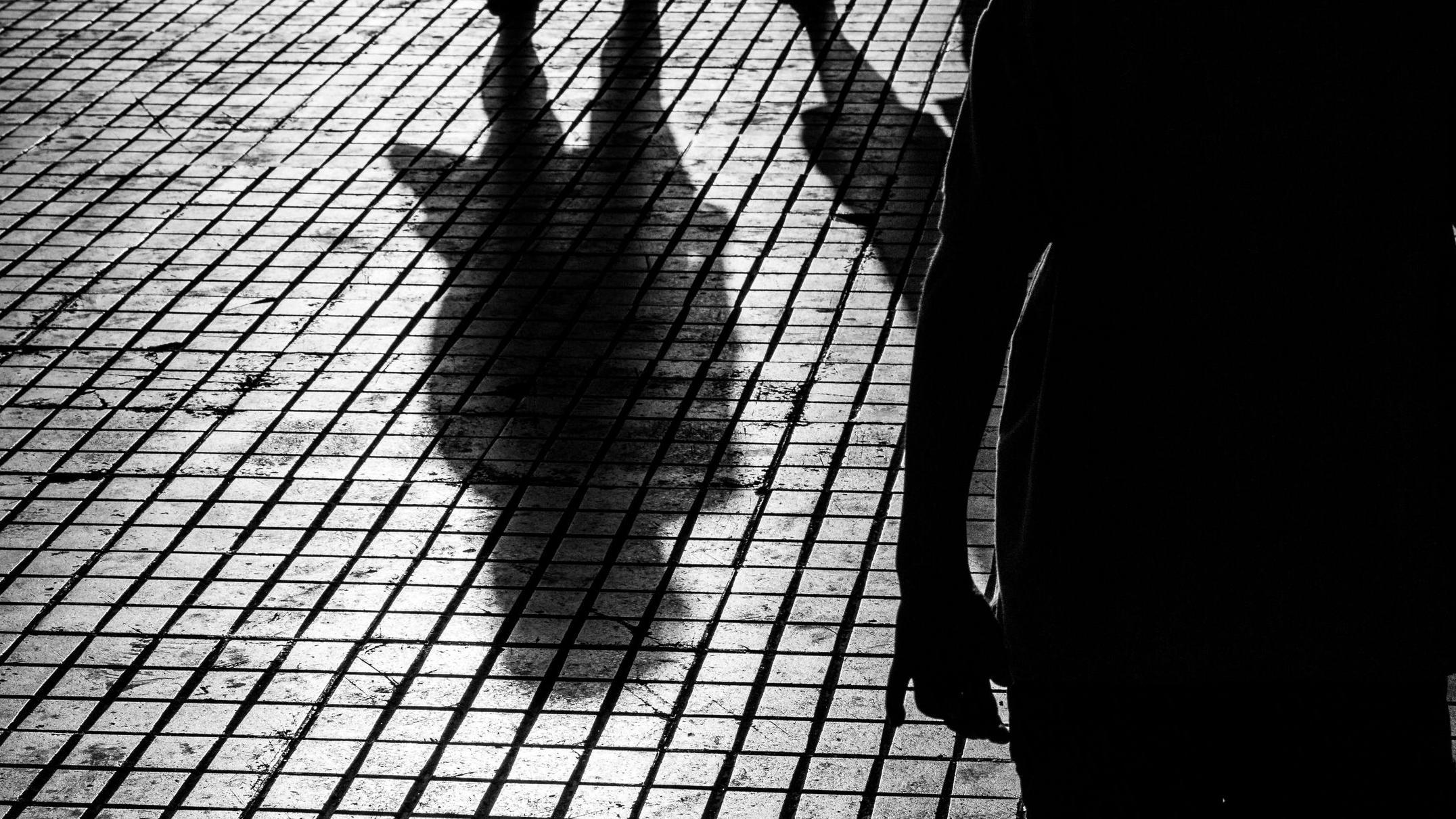 Sombra de mulher andando na rua e pessoa atrás dela