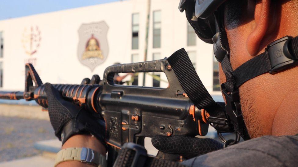 Policial com arma em punho na Universidade de Segurança e Justiça de Tamaulipas.