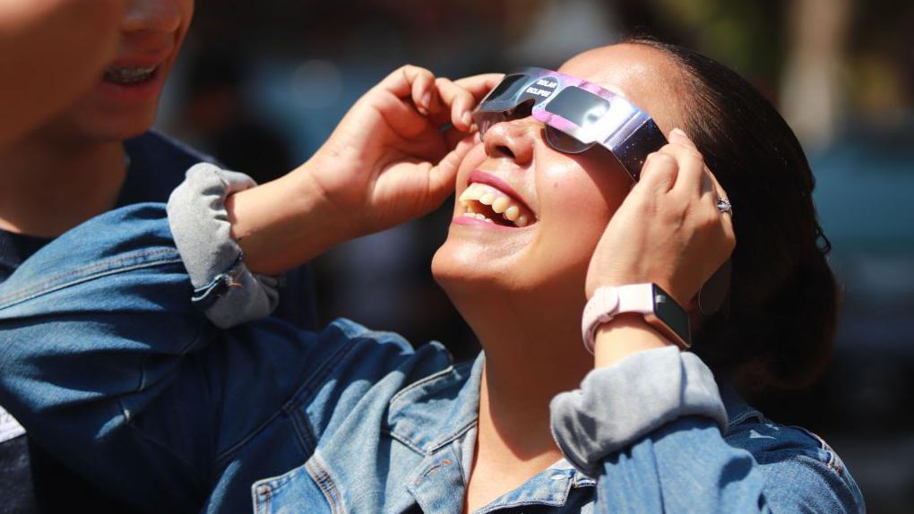 Mulher observa eclipse com óculos de proteção