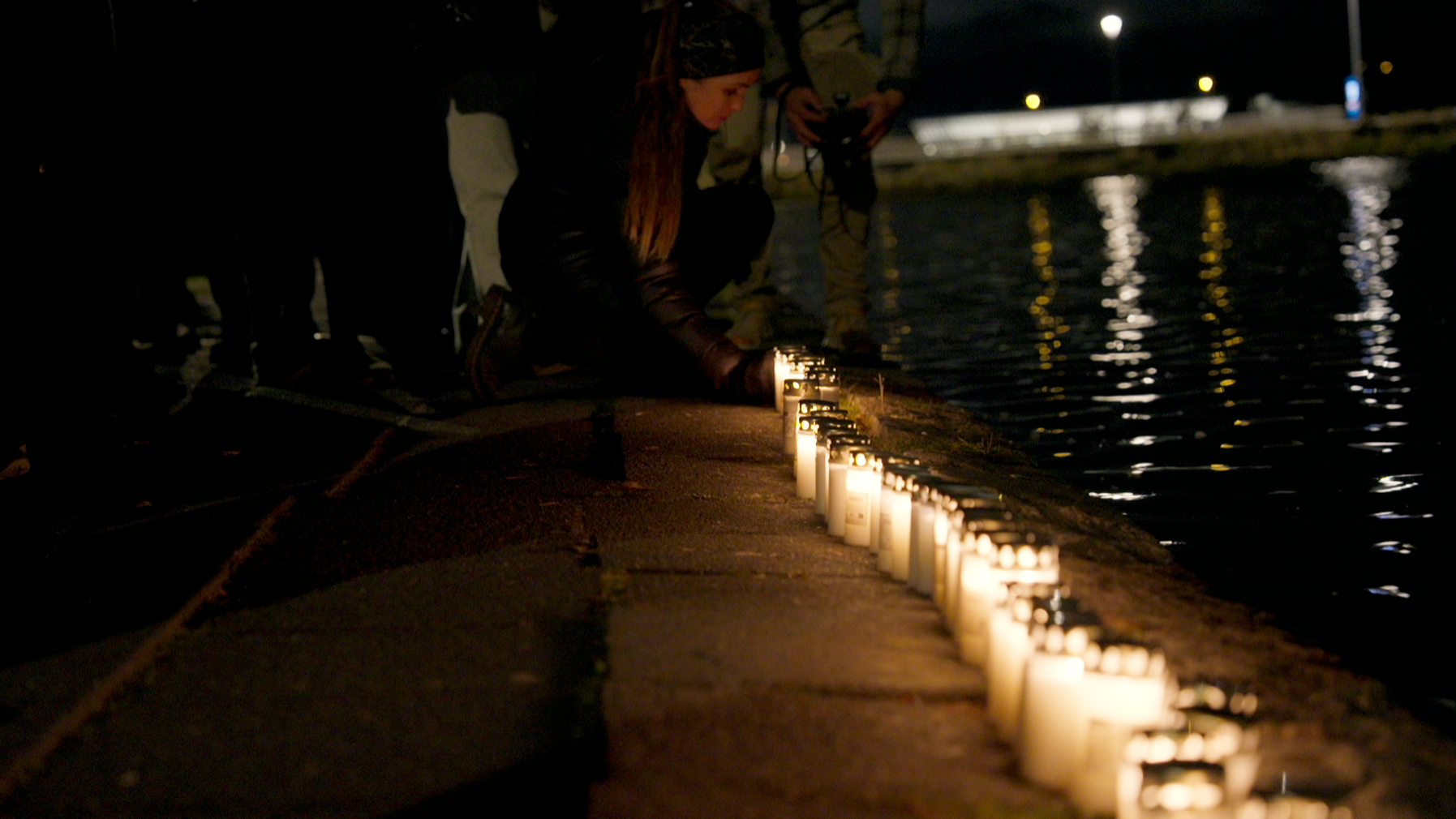 Una persona colocando una vela al lado del río.