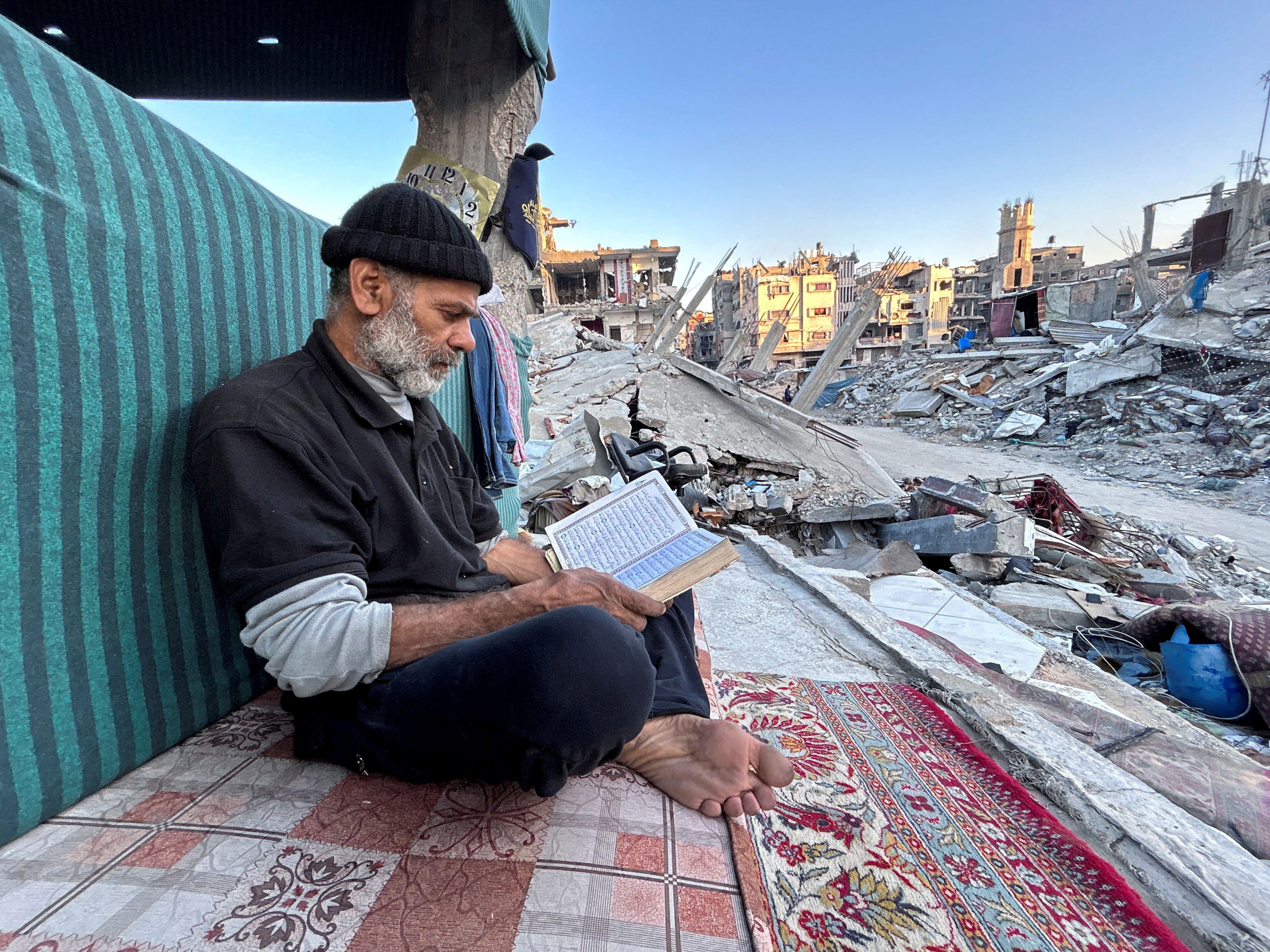 رجل فلسطيني  يقرأ القرآن وهو ينتظر الإفطار بينما يجلس على أنقاض منزله المدمر شمال قطاع غزة
